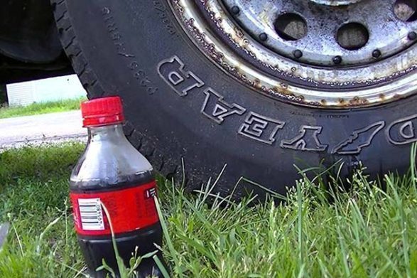 Une bouteille de coca cola assis à côté d'un pneu de voiture