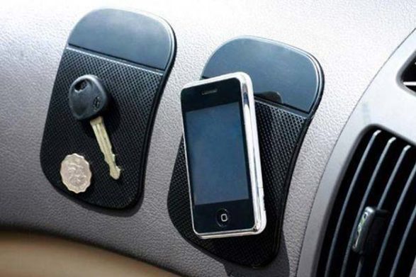 un téléphone, une clé et une pièce de monnaie collées sur des tapis collants sur le tableau de bord d'une voiture