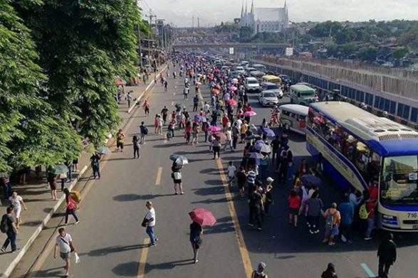 des centaines de personnes marchent le long de l'avenue encombrée du Commonwealth aux Philippines
