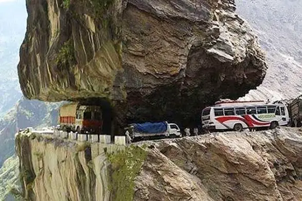 Fahrzeuge fahren unter großen Felsen entlang des Karnali Highway in Indien