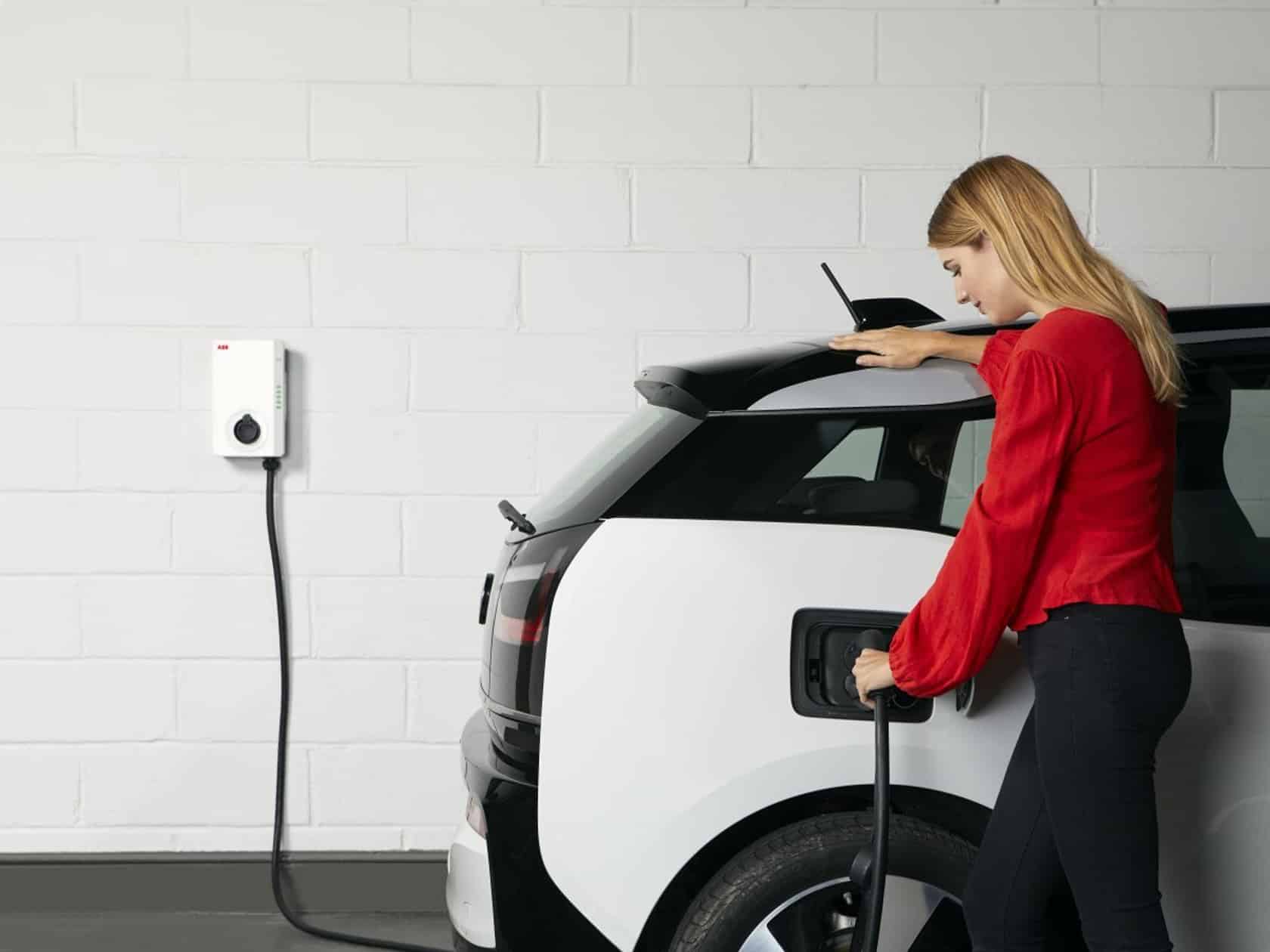 Femme branchant sa voiture électrique sur une borne de recharge murale ABB à domicile